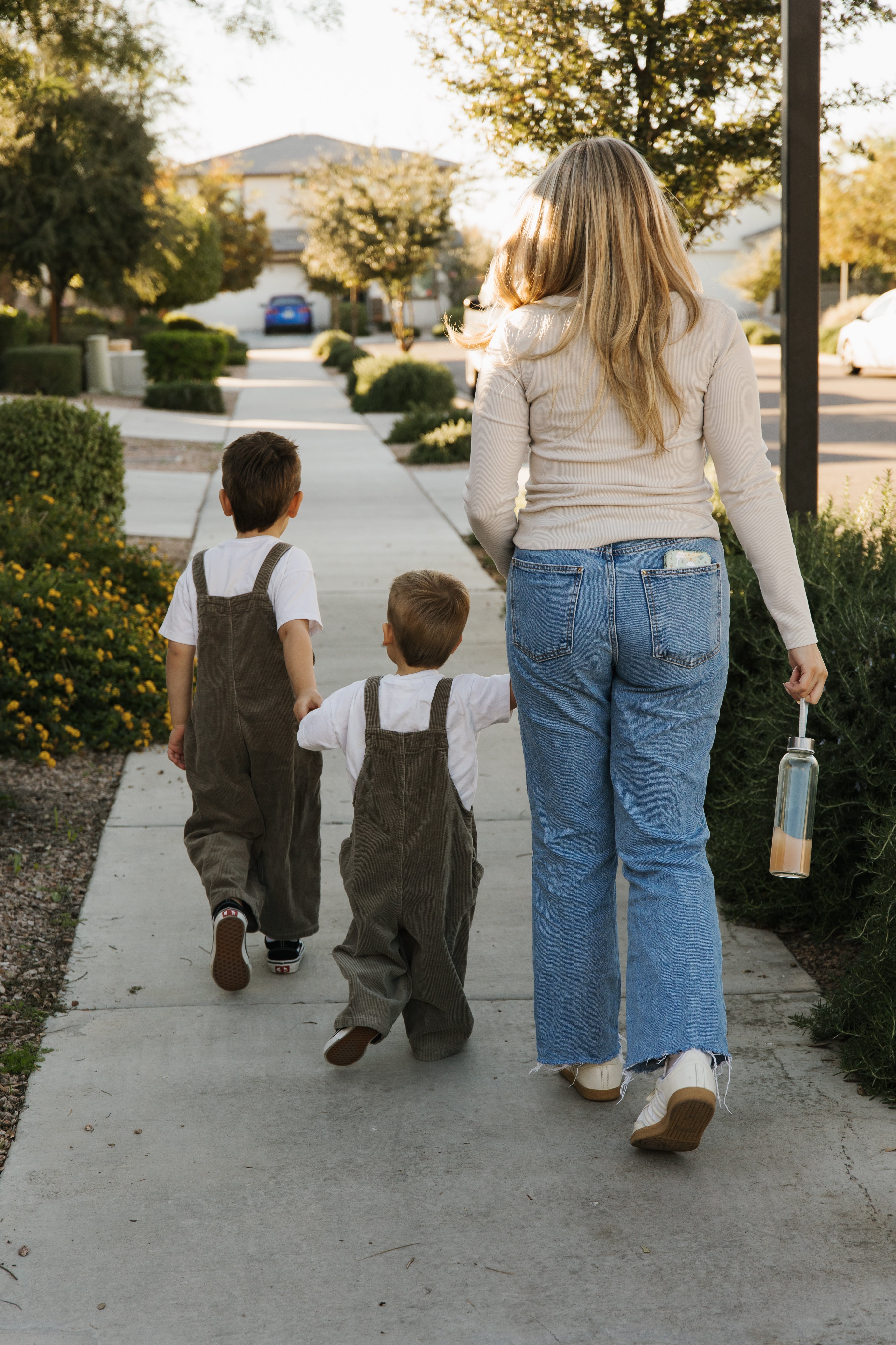 Woman walking with two children on a sidewalk in a suburban neighborhood.